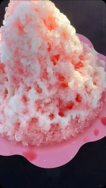 A pink-and-white snow cone on a pink serving tray
