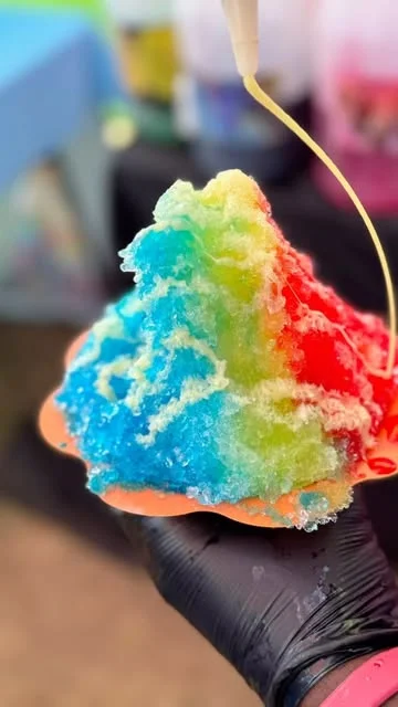 A bright blue, green, and red snow cone getting a finishing drizzle
